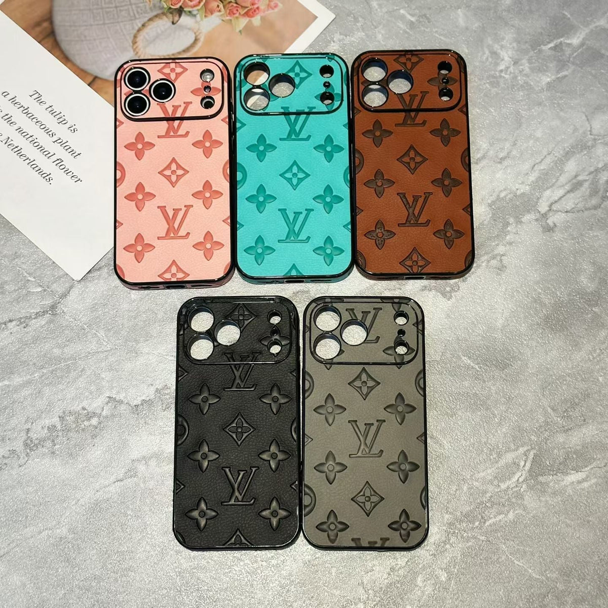 Five Louis Vuitton patterned phone cases on a gray surface.